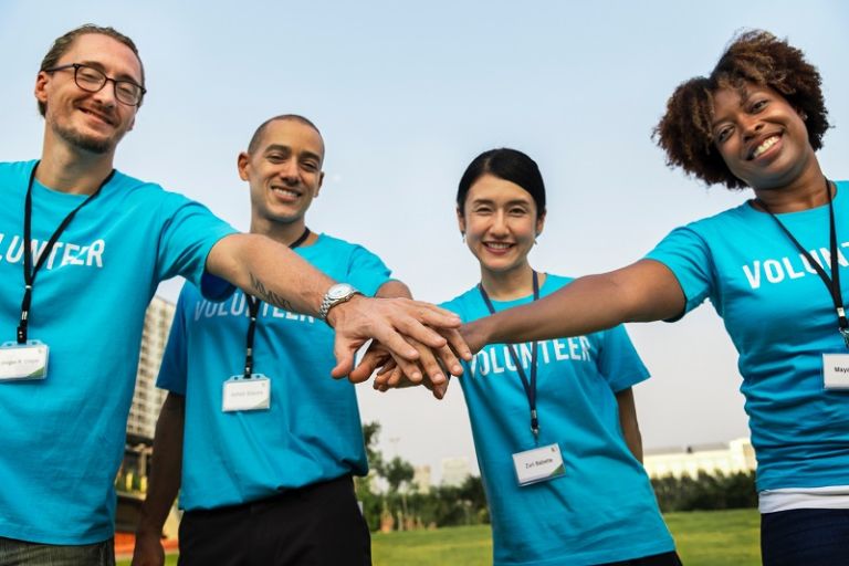 4 Volunteers at an event with hands touching for teamwork