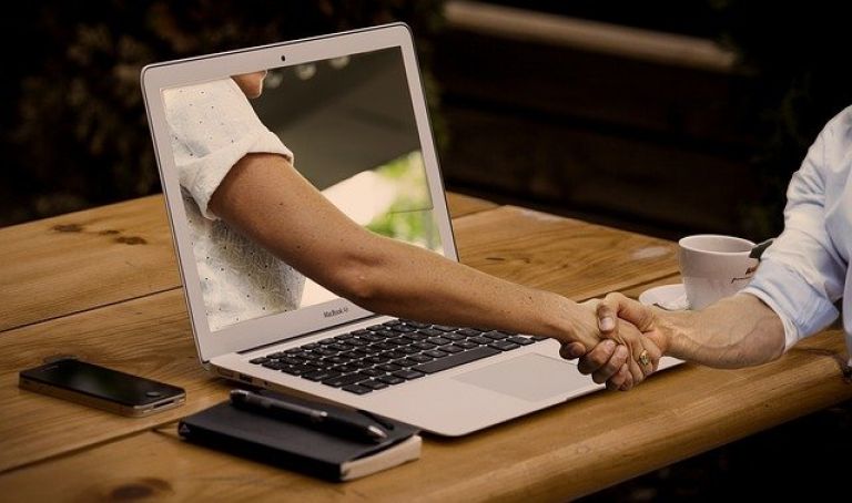 hand reaching through laptop to shake hand of person on the other side of the screen