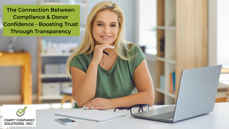 A professional woman with blonde hair is sitting at a desk with a laptop, notebook, smartphone, and a pair of glasses, smiling at the camera. There's a text overlay at the top that reads "The Connection Between Compliance & Donor Confidence - Boosting Trust Through Transparency" and a logo in the bottom left corner for "Charity Compliance Solutions, Inc." The setting appears to be a bright, modern office.