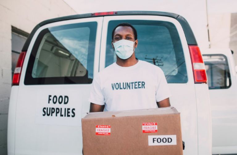 Volunteer wearing a mask carrying food to give out to those in need